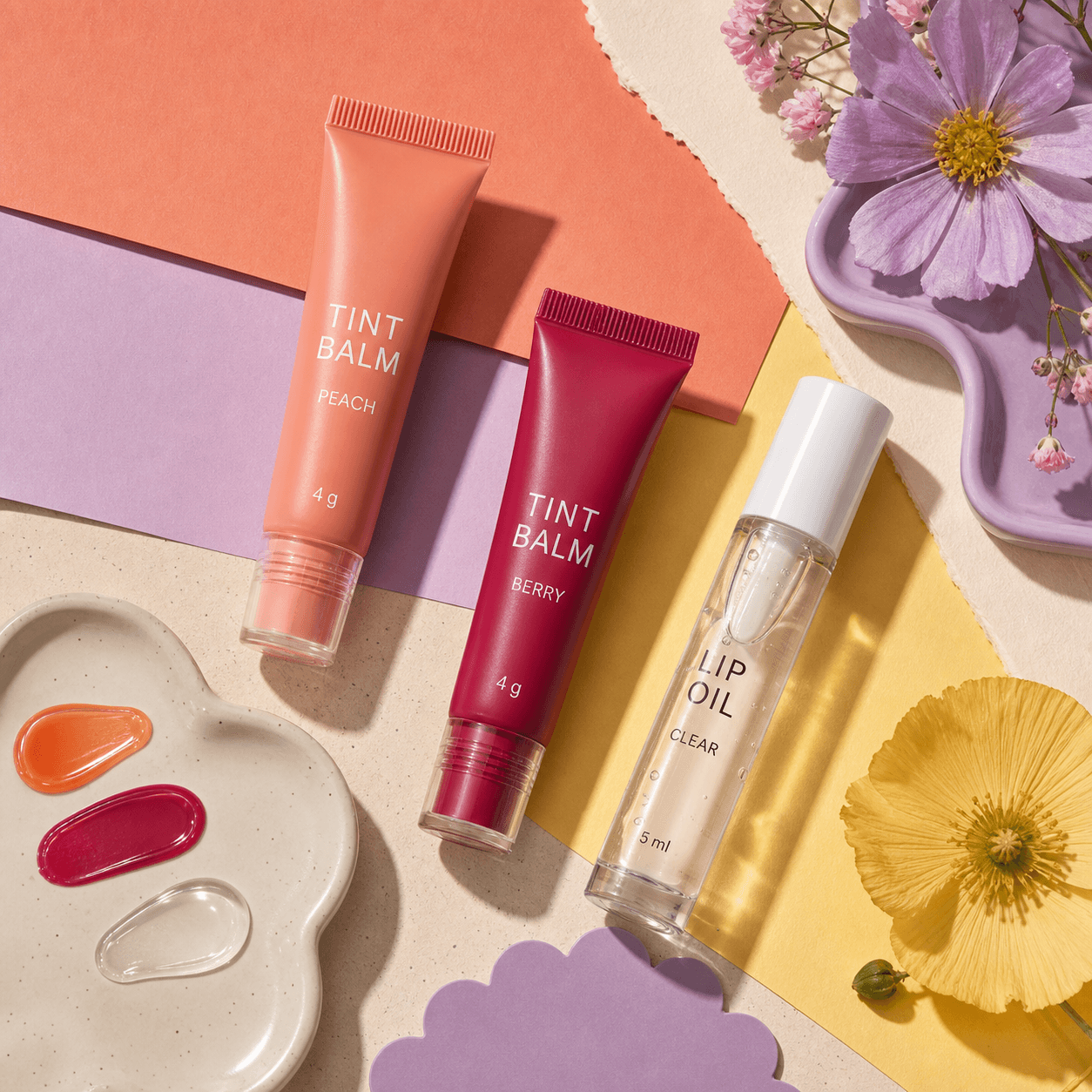 ภาพ flat lay TINT BALM สี PEACH และ BERRY 4 g กับ LIP OIL CLEAR 5 ml พร้อม swatch สามสี