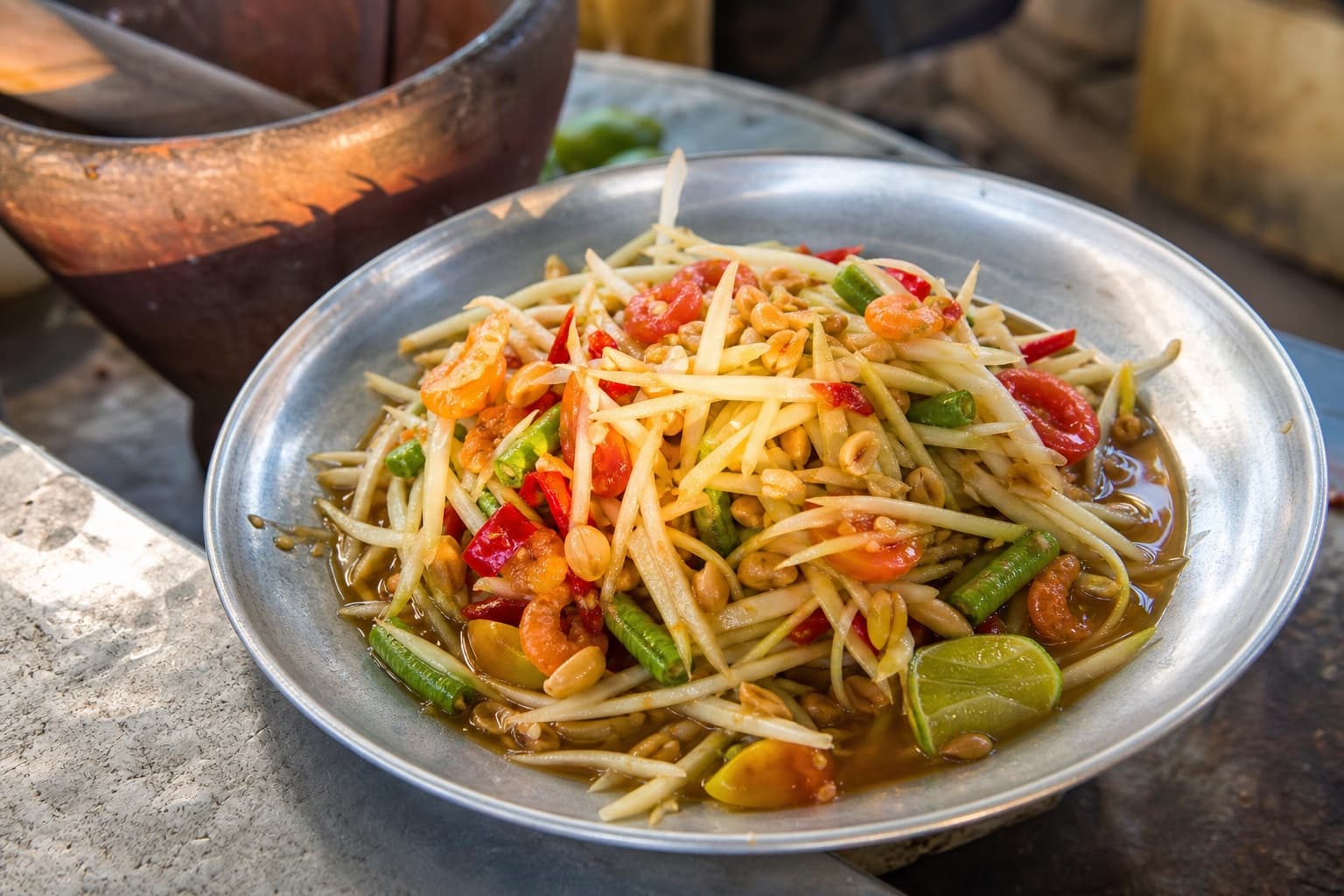 ส้มตำไทยในจานโลหะถ่ายใกล้โต๊ะร้านอาหารสตรีตฟู้ด